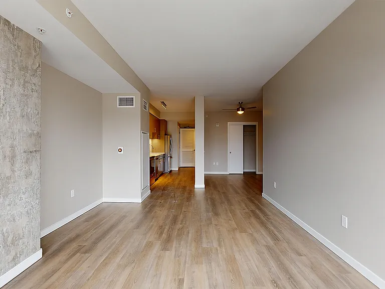 Apartment kitchen with stainless steel appliances, dining and living room with wood-style flooring.
