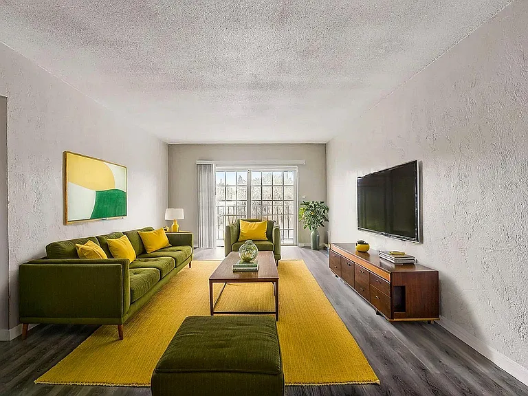 Inviting modern living room with chic green sofas, vibrant yellow accents, and a large window for natural light.