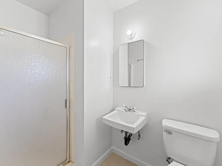 Master bathroom featuring a standing shower with frosted frosted glass door and frosted window for privacy, wall-mounted sink, freshly painted walls, and new tile flooring.