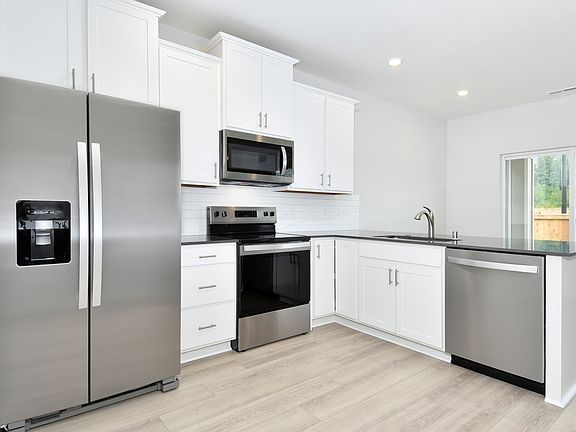 The kitchen has stainless steel appliances and plank flooring.
