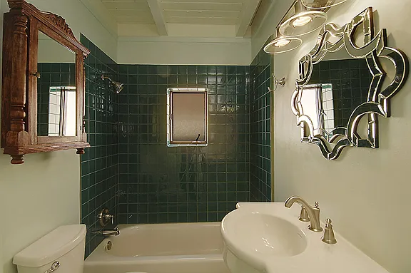 Bathroom showing glass-tiled tub and shower, antique medicine chest and fancy mirror