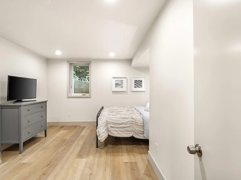 Neat bedroom with hardwood-style floors, recessed lighting, a window, and space for a bed plus dresser and TV.