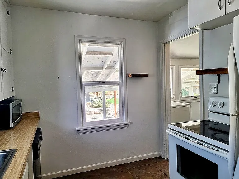 Kitchen with updated stove/range. Notice custom wooden open storage shelving. Doorway on right leads to back porch with washer/dryer. Appliances in kitchen include refrigerator/freezer, dishwasher, garbage disposal, electric stovetop/oven.