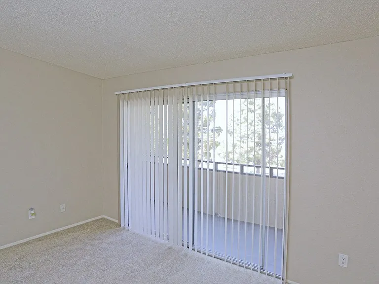 Carpeted master bedroom with sliding glass door to private porch at Villa Pacific Apartments in Oceanside, California.