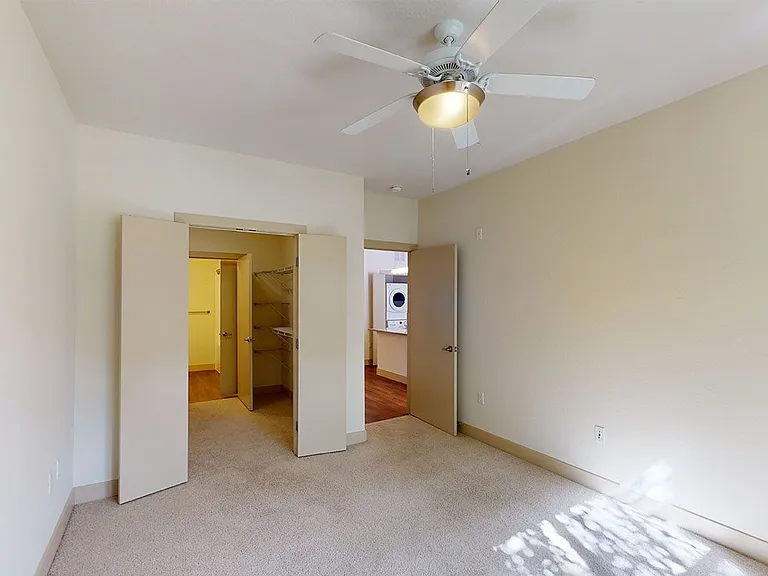 Spacious apartment bedroom with large closet, attached bathroom and plush carpet flooring.