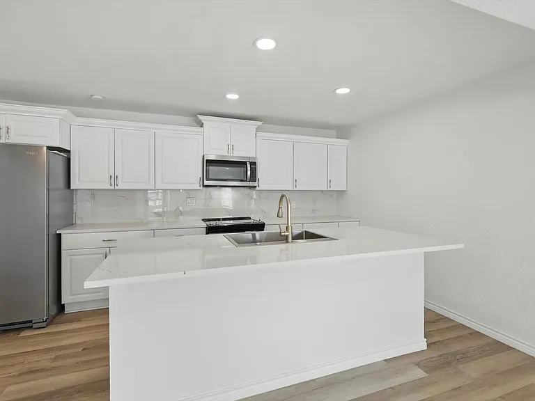 Kitchen with stainless steel appliances, a sink, white cabinetry, light countertops, and recessed lighting