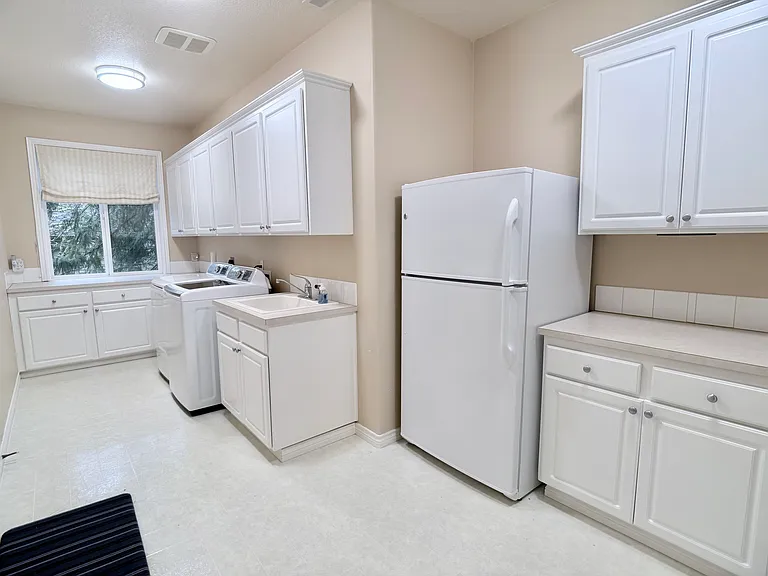 Spacious, fully equipped laundry room featuring abundant storage, a utility sink, washer and dryer, secondary refrigerator and generous counter space.