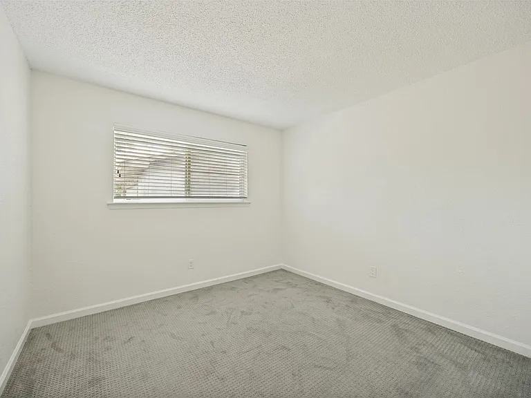 Neutral interior room featuring a window with horizontal blinds, light-toned walls, and a textured ceiling