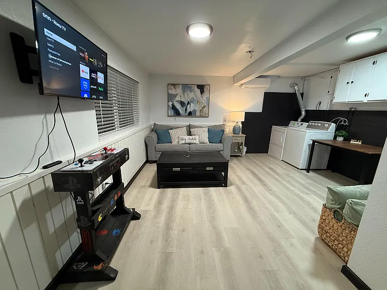 Open-concept common area with seating, wall-mounted TV, and adjacent laundry plus cabinet storage and work surface.