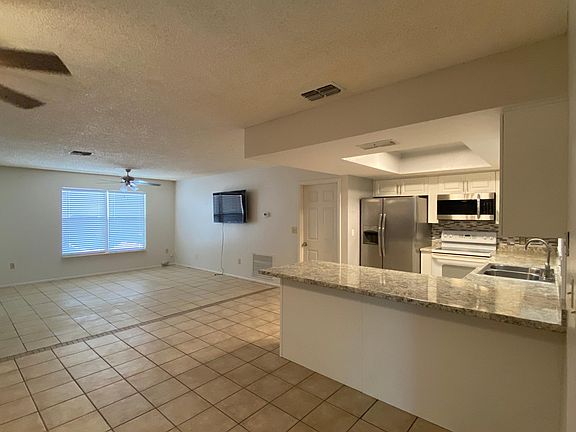Living room with ceiling fan and front door. Side view of door to laundry room and third bedroom and bathroom.