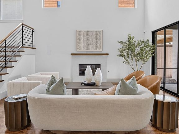 Double-height living space featuring a fireplace, wood-finish flooring, a contemporary staircase with iron balusters, and expansive glass doors