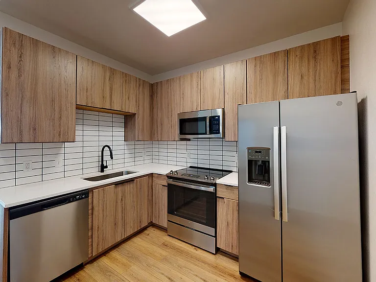 Apartment kitchen with stainless steel appliances, quartz countertops and wood-style flooring.