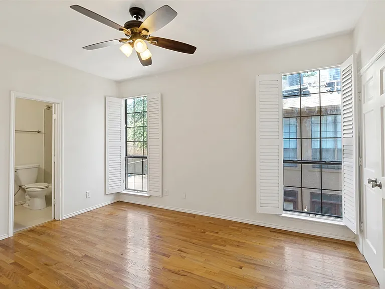 Wood-finish flooring, two windows with louvered shutters, ceiling fan with integrated lighting, white interior doors