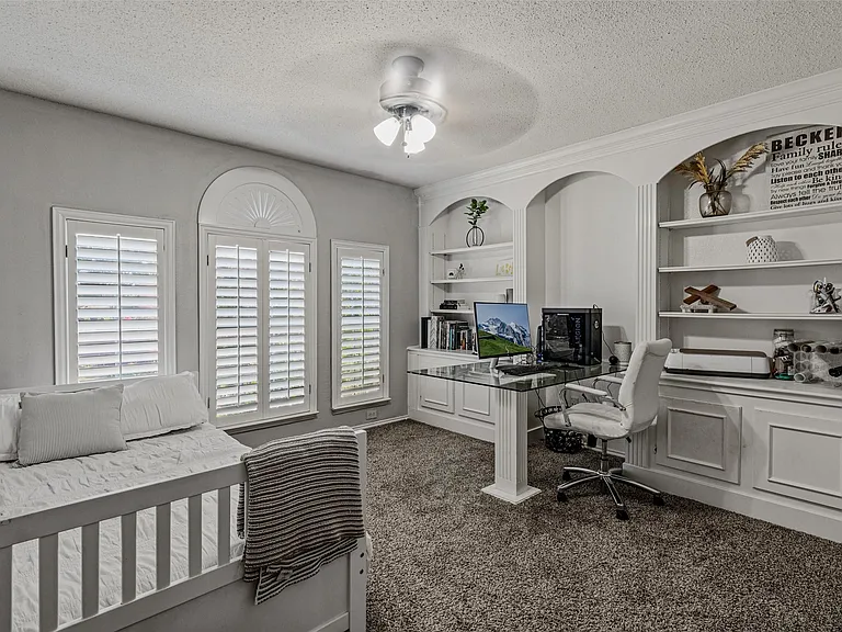 Room featuring built-in shelving, an arched transom window, shuttered windows, a ceiling fan, and carpet flooring