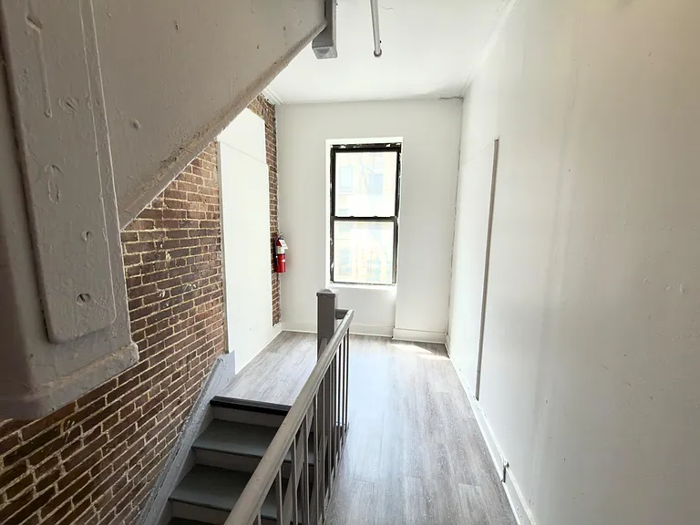 Sunlit stair landing with exposed brick accent, durable flooring, and a window that brings in natural light.