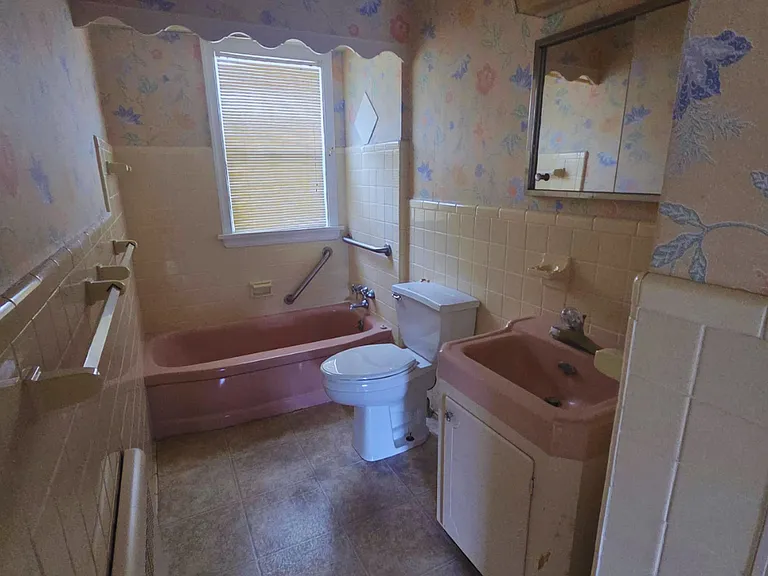 Bright spacious bathroom with floral walls, tub, sink, mirror & towel racks