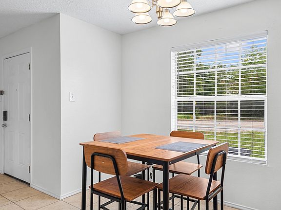 Dining area with a four-seat table set beside a large window with blinds, plus an overhead light for everyday meals.
