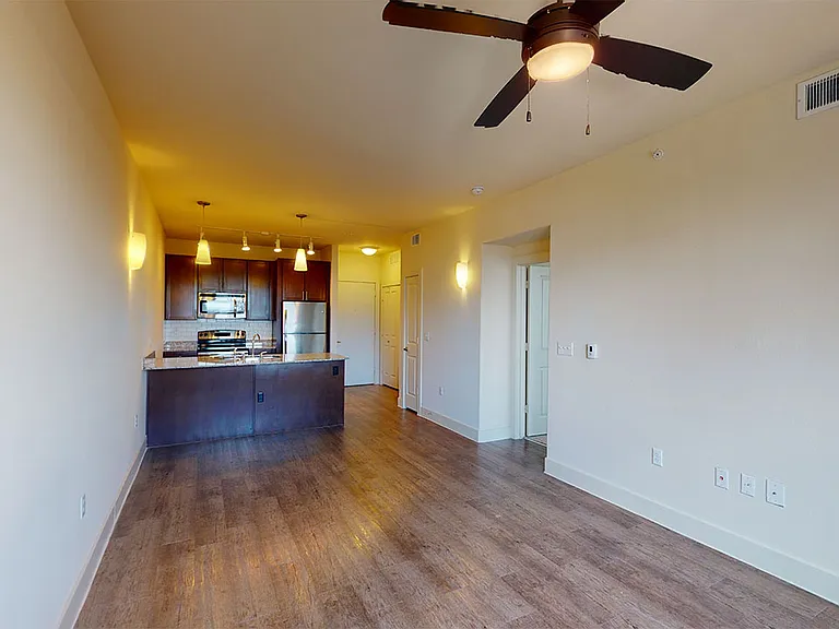 Apartment kitchen with stainless steel appliances in select homes, dining and living room with wood-style flooring.