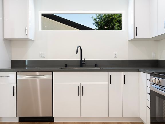 Brand new modern kitchen with sleek white cabinets, black quartz countertops, and top-of-the-line stainless steel appliances.