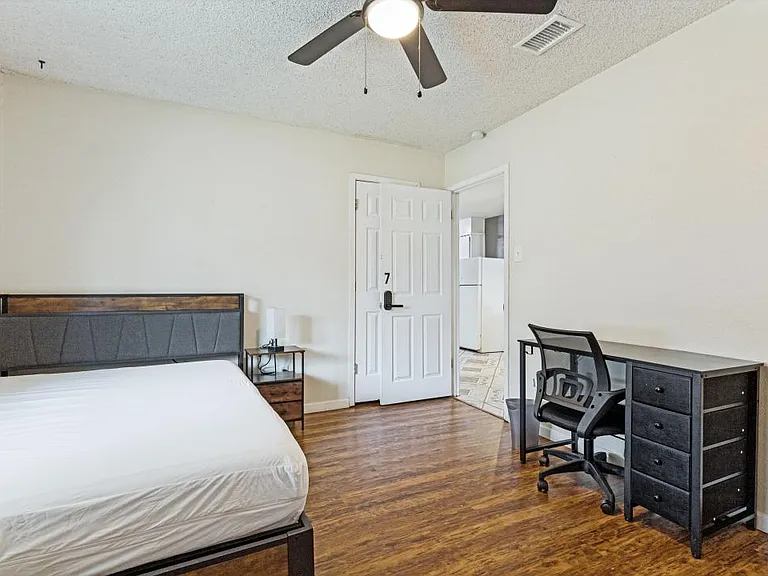 Spacious bedroom with wood-look floors, ceiling fan, and room for a full bed plus a desk or seating area.