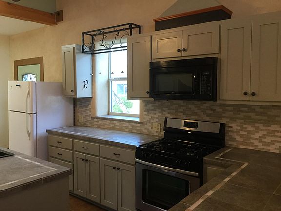 Kitchen has tile counters, glass tile backsplash, gas range, built in microwave, island.