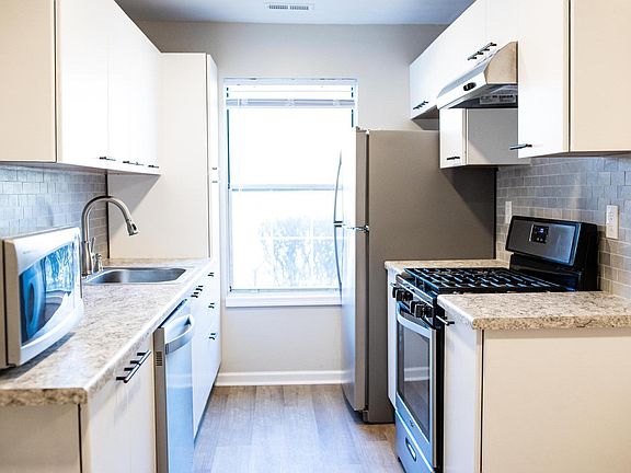 Galley style kitchen with new countertops, backsplash, freshly painted white cabinets, new dishwasher and sink, and recent refrigerator and stove.