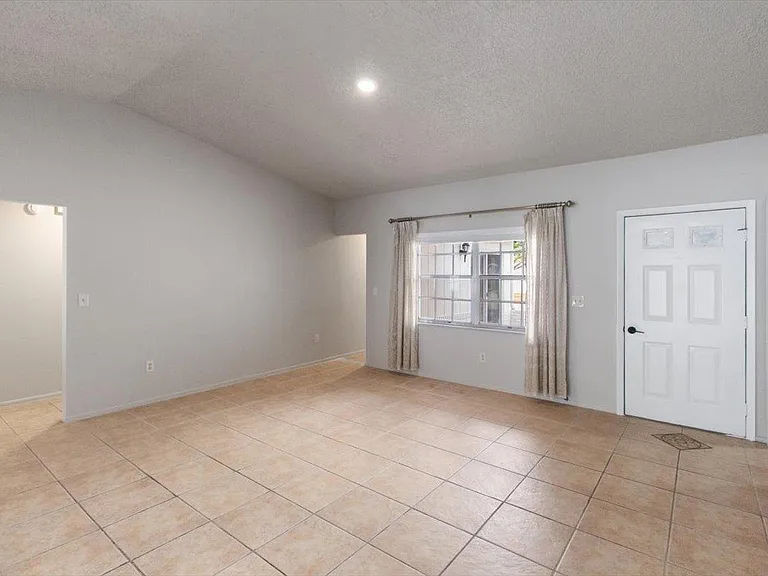 Open living area with tile flooring, large window with curtains, and ample wall space for flexible seating arrangements.