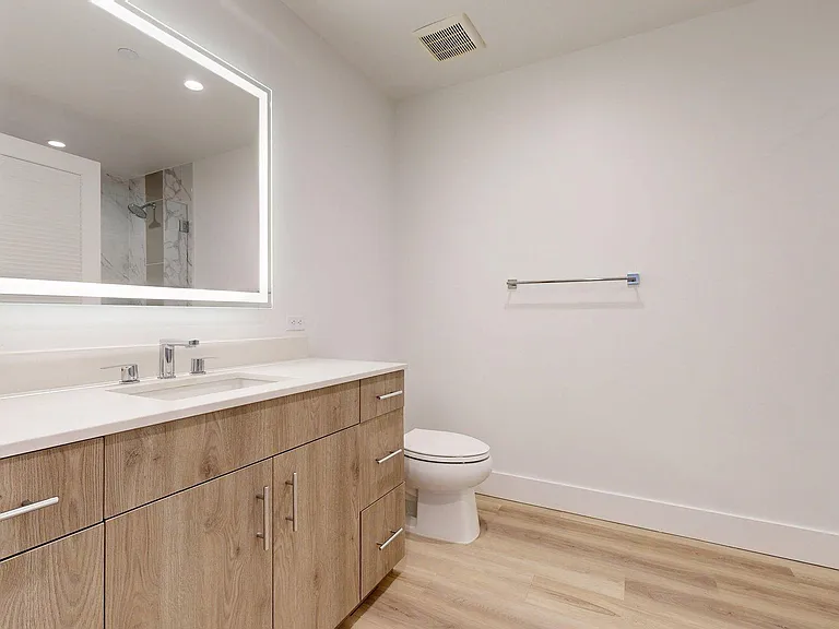Apartment Bathroom with glass enclosed shower, LED vanity mirror and Wood Style Flooring.