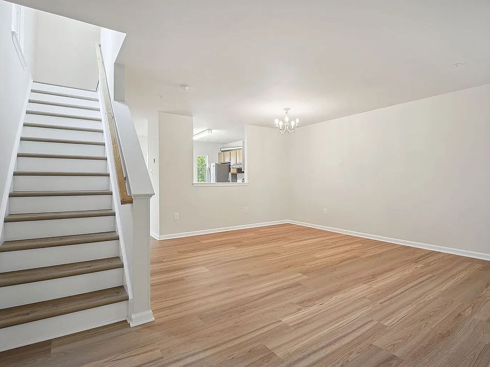 The view of the living and dining area upon entering the unit. The kitchen is visible beyond through the pass-through opening. The stairs to the upper level are on the left.