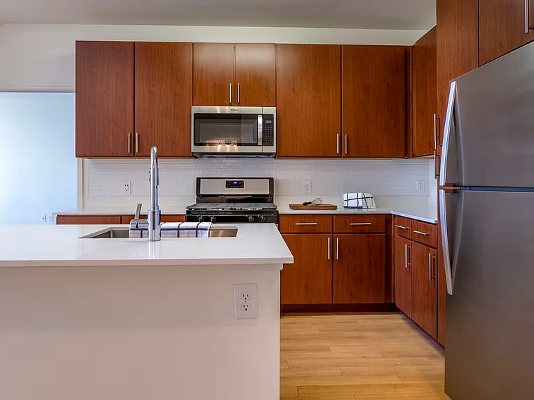 Newly renovated apartment homes feature kitchens with cherry cabinetry, white quartz countertops, stainless steel appliances, white tile backsplash, and hard surface flooring