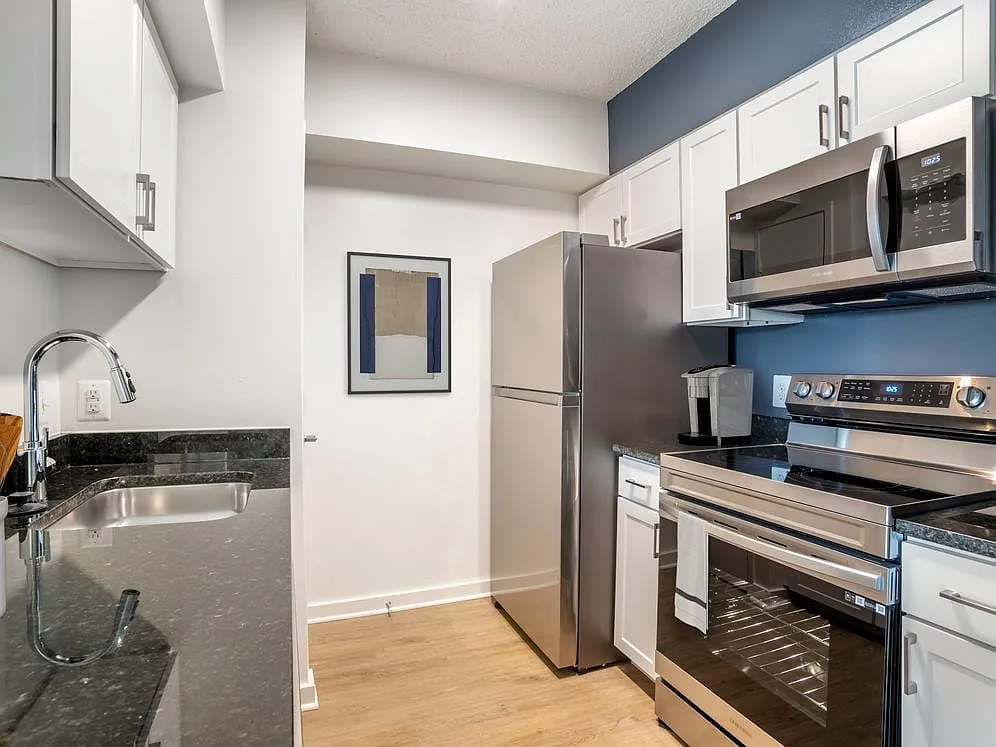Renovated Package II kitchen with stainless steel appliances, white shaker cabinetry, dark speckled granite countertops, and hard surface flooring - AVA Ballston
