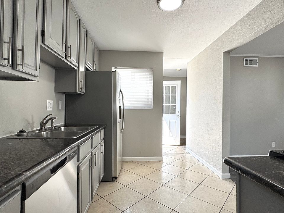 Bright, modern kitchen with sleek grey cabinets, stainless steel appliances, and elegant tile flooring, opening to a sunlit entryway.