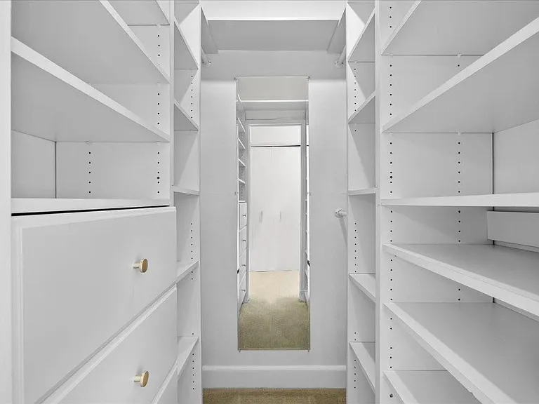 Expansive walk-in closet with custom built-ins, hanging space, mirror, drawers, and shelving.