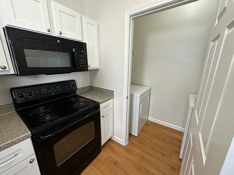 Modern kitchen featuring sleek black appliances, elegant white cabinetry, and adjacent laundry area with washer and dryer. Modern kitchen featuring sleek black appliances, elegant white cabinetry, and adjacent laundry area with washer and dryer.