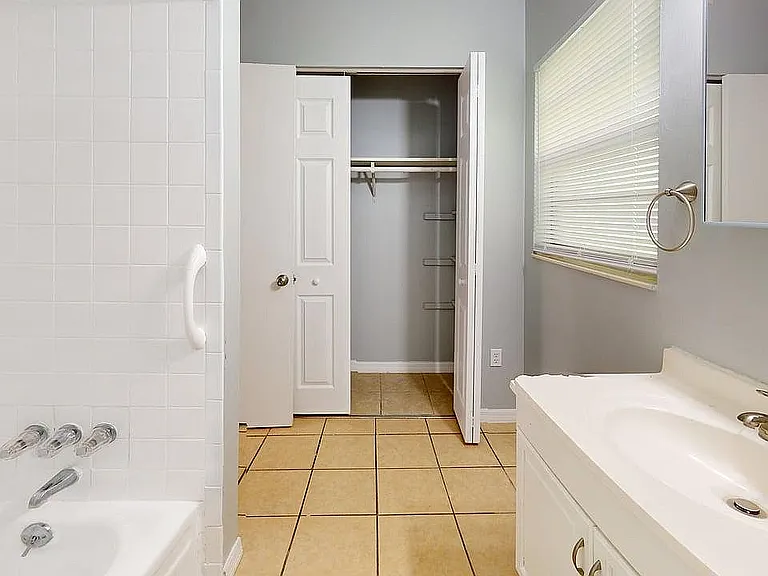 Bright and spacious bathroom featuring a pristine white bathtub, elegant vanity, and convenient closet space.
