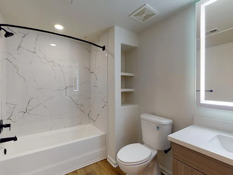 Apartment bathroom with wood-style flooring and LED vanity mirror.
