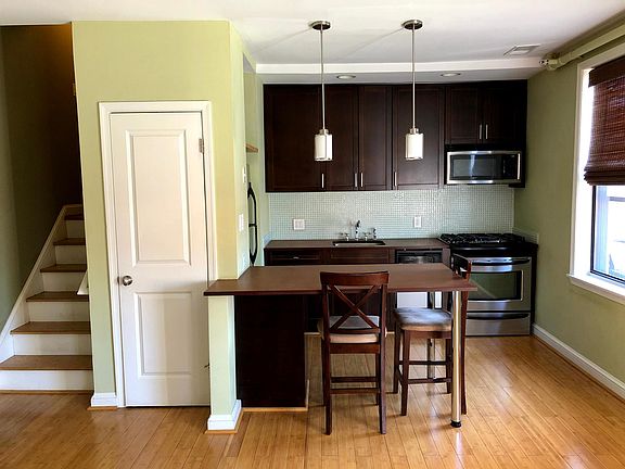 Kitchen viewed from Fireplace. White door shown is a pantry with shelves. Unit Entrance to the left, up the small flight of stairs (plenty wide for furniture moving)