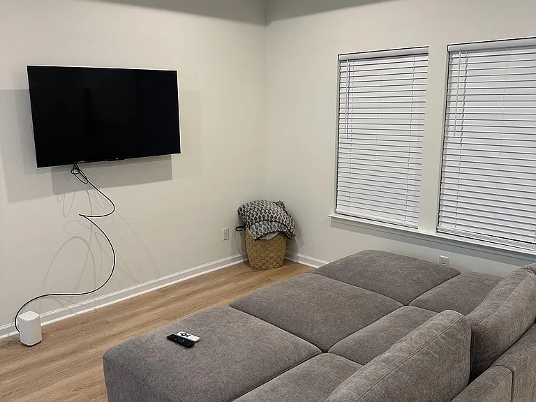Shared living room with a sectional sofa, wall-mounted TV, and large windows with blinds for comfortable lounging.