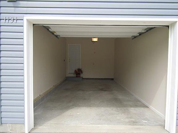 Deep garage with automatic remote, cream walls and cement floor, light bulb and motor lights.