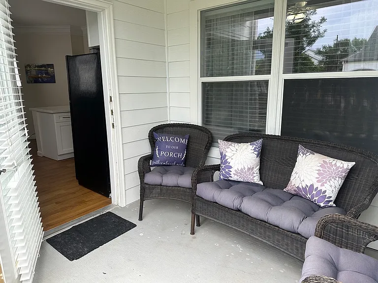 Inviting porch with cozy wicker seating and floral cushions, leading into a bright kitchen. Inviting porch with cozy wicker seating and floral cushions, leading into a bright kitchen.