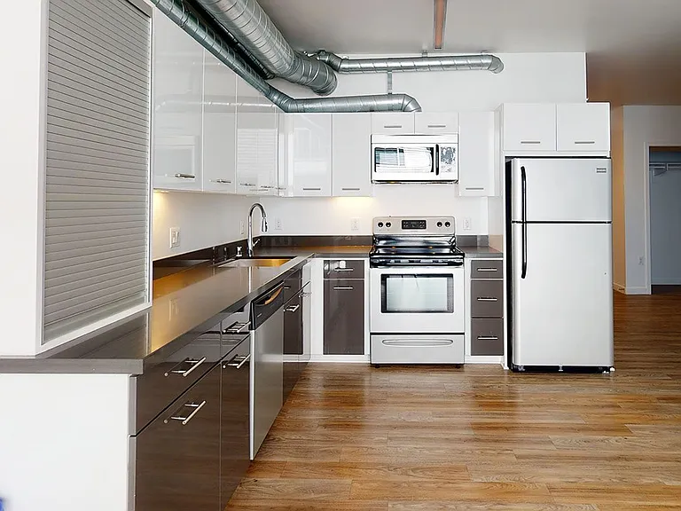 Apartment kitchen with stainless steel appliances, quartz countertops and wood-style flooring.