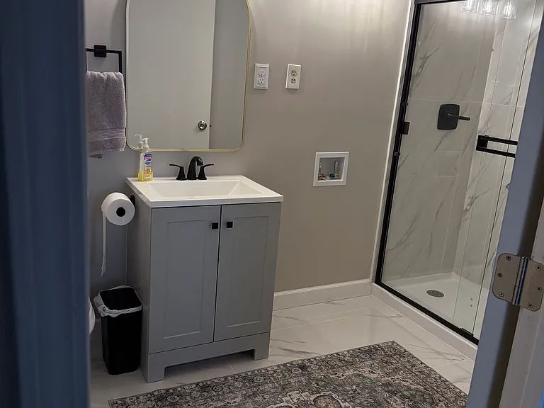 This updated full bathroom features a clean, modern design with a stylish vanity, contemporary lighting, and a spacious glass-enclosed walk-in shower with beautiful tile detailing.