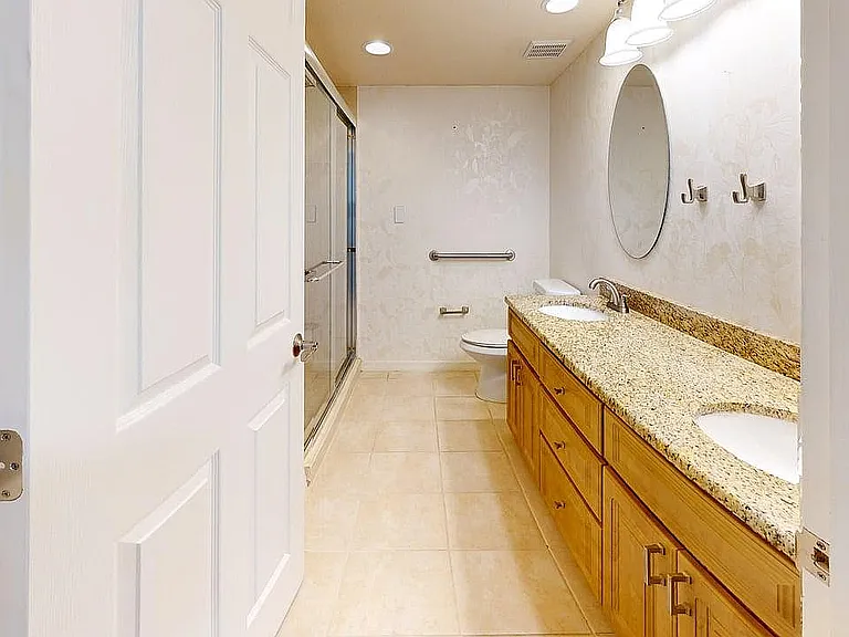 Bright and spacious bathroom showcasing a luxurious granite double vanity, elegant lighting, and a stylish walk-in shower.