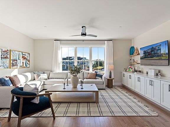 Bright living room with a large sectional sofa, armchair, TV, and large windows letting in natural l