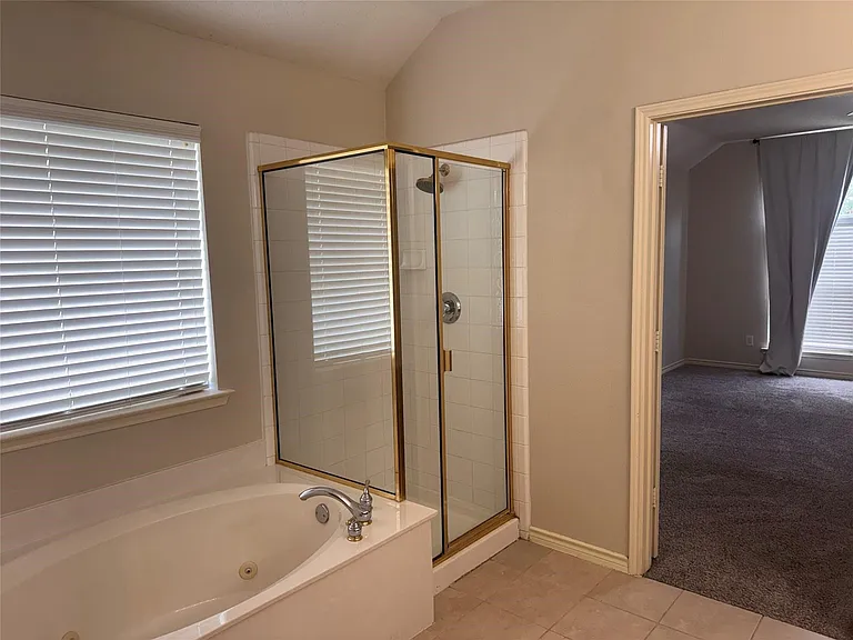 Soaking tub with integrated jets, framed glass shower enclosure with gold-tone accents, tiled flooring, and neutral wall paint