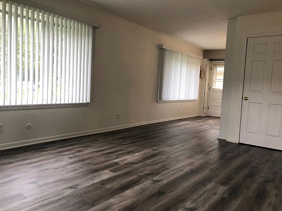 Living room with new floors opens into eat-in kitchen. Bay windows. Door is a coat closet with hanging rack and plenty of floor space.