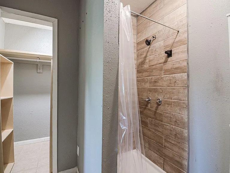 Bathroom with a walk-in shower featuring tile surround, plus adjacent storage shelving and closet space.