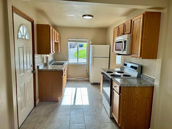 Front door opens into the kitchen. The kitchen features a refrigerator, double sink, electric stove, and microwave range.