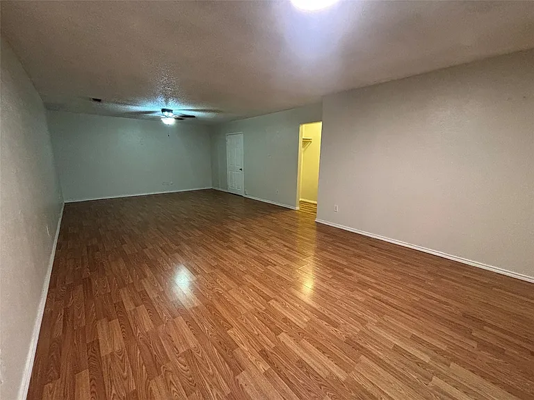 Spacious room featuring wood-finish flooring, light neutral wall paint, and a ceiling-mounted light fixture with fan