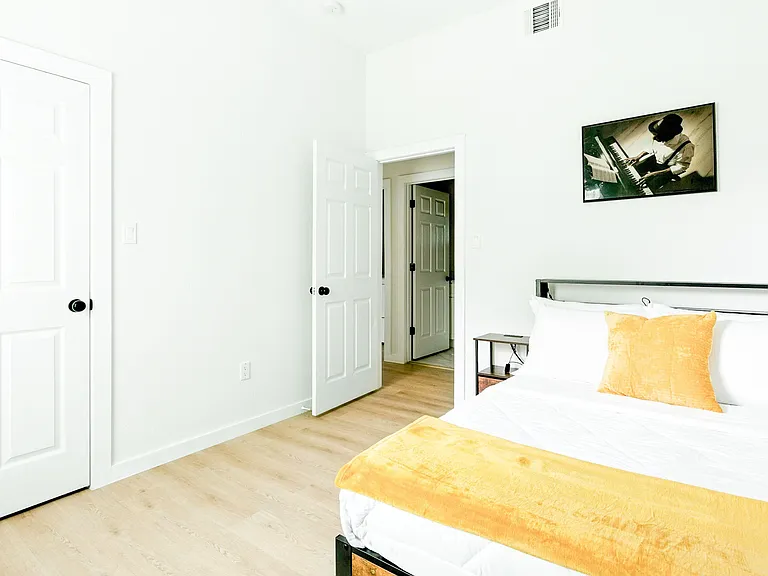 Furnished bedroom with a full/queen bed, side table, and wood-look flooring, plus easy access to the hallway.